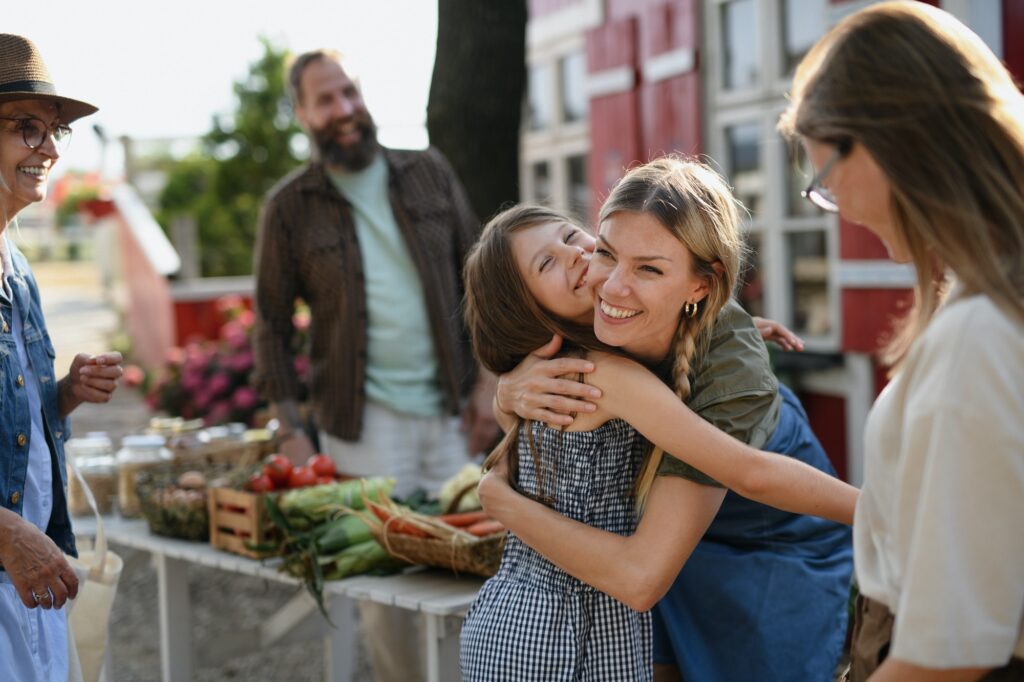 Little girl with mother hugging outdoors at community farmers market